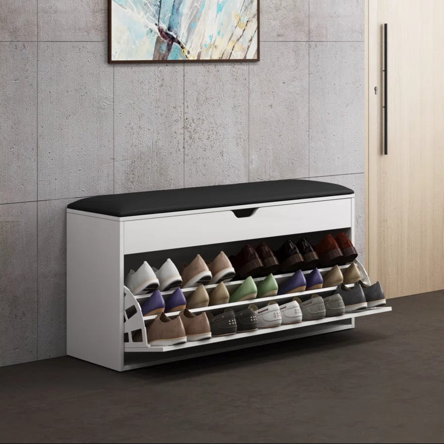 White shoe cabinet with black top holding various shoes against a gray wall with abstract art.