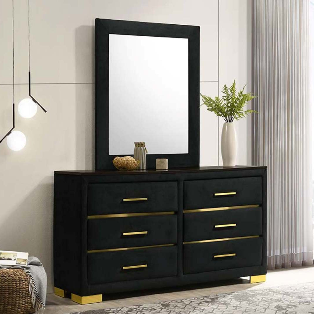 Black dresser with gold handles and a matching mirror in a room with a light gray wall and large window.