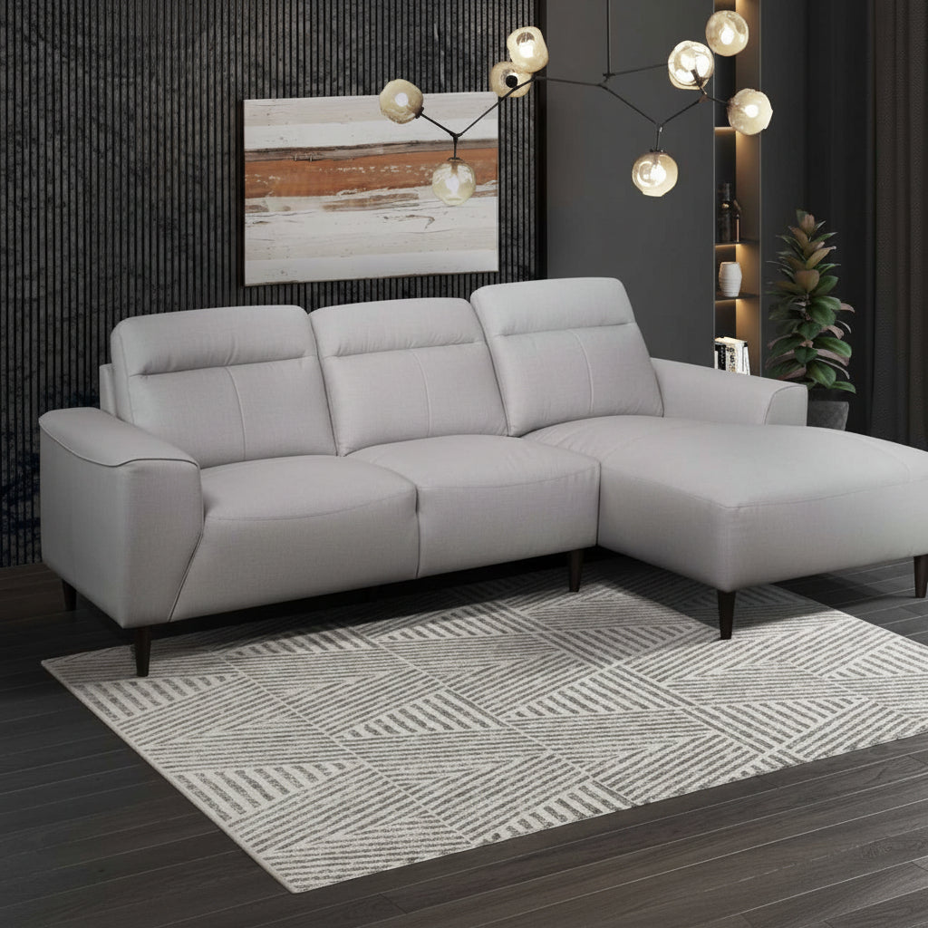 A modern light grey leather sectional sofa with a right side chaise, featuring wide track arms and dark brown wooden legs, set in a room with a striped wall and a framed picture on the wall.