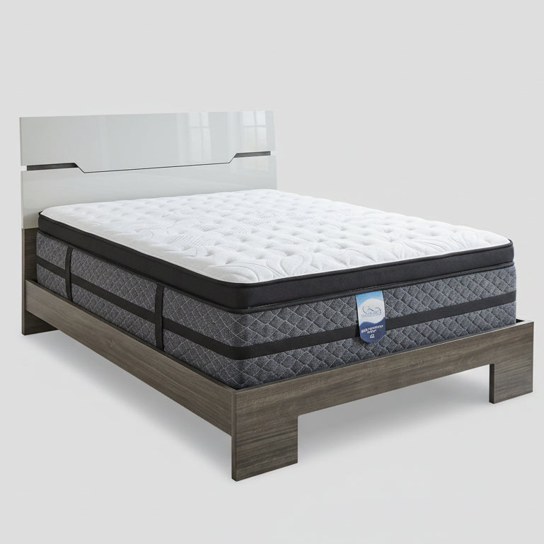 Mattress on a wooden bed frame in a bedroom setting with a lamp and nightstand.